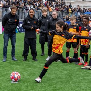 Adults look on as a child kicks a soccer ball.