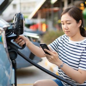a person looks at their phone while plugging in their vehicle
