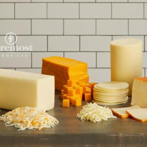 An arrangement of different cheeses and milk on a wood table.