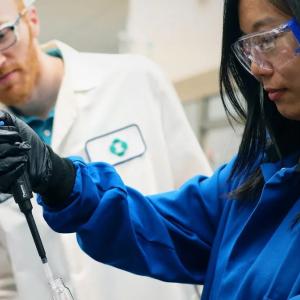 Two chemists, one observing another using a pipette.