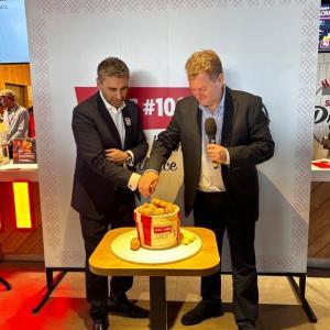 Two people cutting a cake in the shape of a KFC bucket of chicken.
