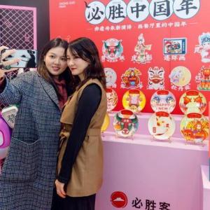 two people take a selfie in front of a display of plates and posters