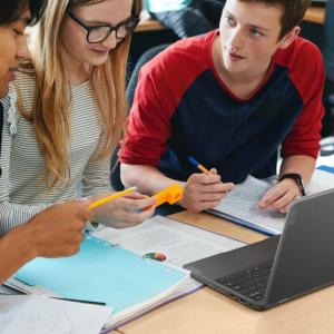 Students working together at a desk, an open laptop between them.