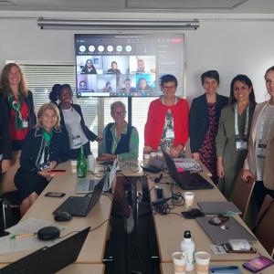 A small team in a conference room, a screen up with virtual participants.