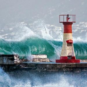 Tall waves crashing over a wall with beacon.