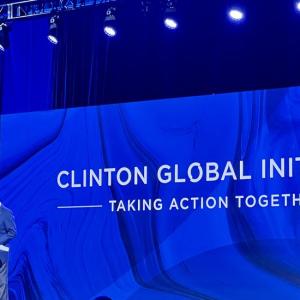Bill Clinton at a podium, a large screen with "Clinton Global Initiative" behind him