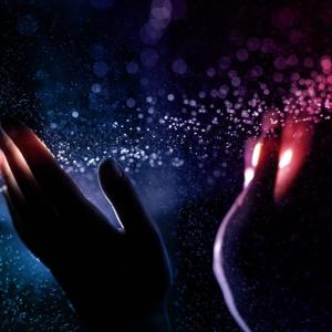 Two dimly lit hands in a colorful cloud of dust.