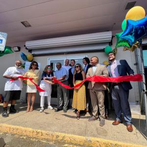 A group of people posed behind a red ribbon outside the doors of the kitchen.