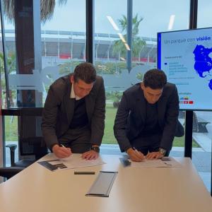 Two people signing a paper on a desk in front of a big window