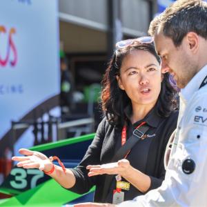 Two people talking, a race car behind them.