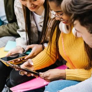 People seated on a bench, looking at each other's phones.