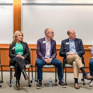 A row of seated people. One speaking. Whiteboards behind them.