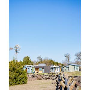 A fence line leading to a group of tiny homes. An old wind vane next to them.
