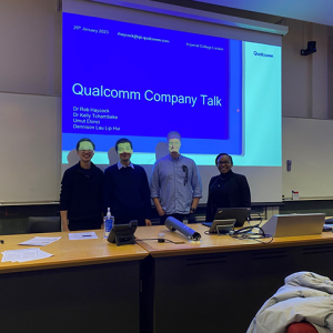 Kelly and others standing in front of a projected presentation, a long desk in front of them.
