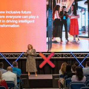 person speaking on stage, some of the audience visible in the front seats