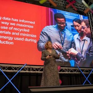 a person speaking on stage with a large projection screen behind them