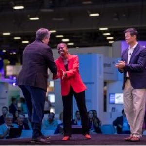 Tracey Brown shaking hands with another. A third person nearby clapping.