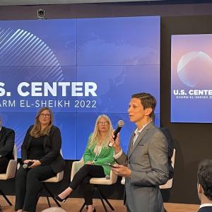 A speaker with microphone, three others seated on stage.