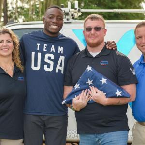 Four people posed together, one holding a folded flag.