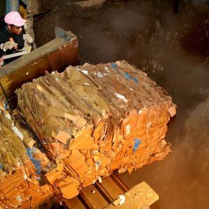 A person watchin as bales of compressed paper travels on a conveyor to a collection pit.