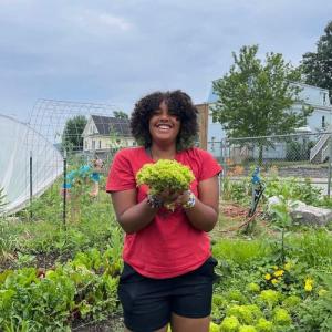 A smiling person holding a bundle of produce outside in a garden.