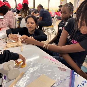 Adult volunteers and children working on building model structures with craft supplies.