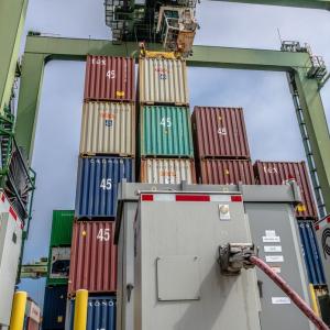 Stacked shipping containers and cranes, power boxes in front.