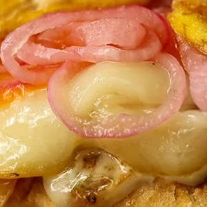 Close up of a chicken sandwich with melted cheese, red onions, and other ingredients.