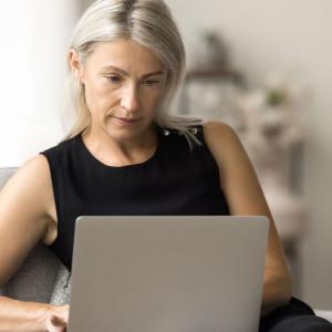 Woman seated at a table reviewing a laptop.