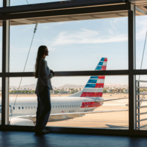 A person, standing, looking out a large window at planes parked outside.