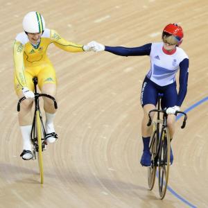 two cyclists on a wooden floor hold hands as they're riding