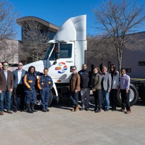 A group of people posed outside in front of a semi truck.