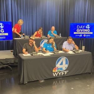 Volunteers on phones during a fundraising event. "Day 4 giving" on screens beside them.