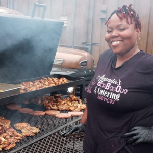 Amanda Kinsey-Joplin in a black t-shirt standing in front of a large barbecue smoker