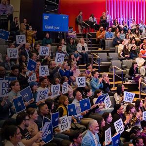 Crowd sitting in a theater at DE&I Day holding signs