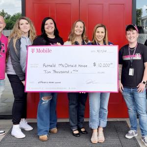 A small group posed with a large check outside a building