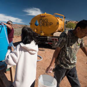 People filling buckets from a large blue container. A tank to the right with "Dig Deep" on the side.