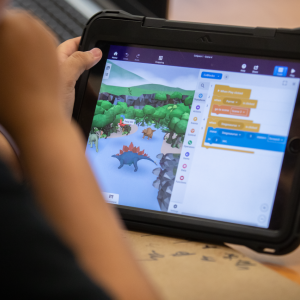 A young child looking at a tablet open to a screen with dinosaurs and text