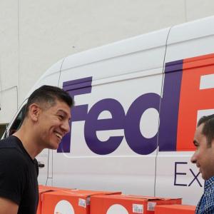 Two people talking and smiling next to a FedEx Express van and Direct Relief boxes