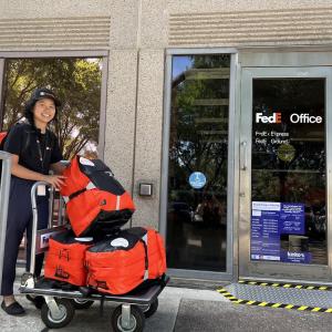 Someone rolling red bags on a trolley to a FedEx office