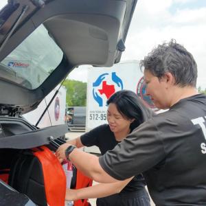 Two people putting red bags into a vehicle trunk