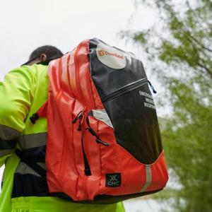 Two people wearing high-vis jackets and backpacks walking outside.