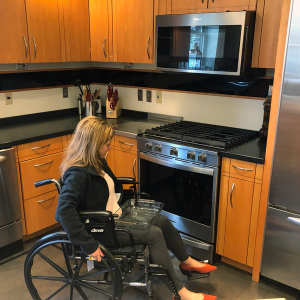 woman in a wheelchair approaching an oven with a glass casserole dish on her lap