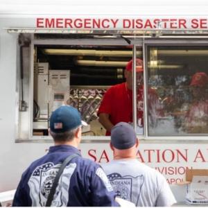 Three people in line in front of a food truck "Emergency disaster services" and Salvation army logos.