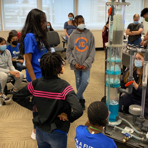 a volunteer shows a group of children how the distillation tower model works