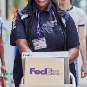 A person in FedEx uniform wheeling a stack of boxes on a dolly.