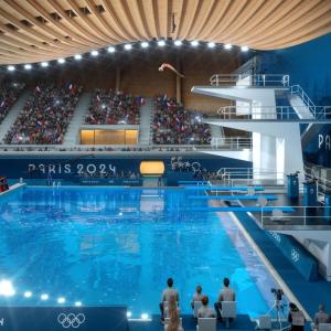 A person diving from a high platform in an aquatics center. People in the stands watching.