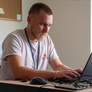 A person seated, working on a laptop in an office setting.