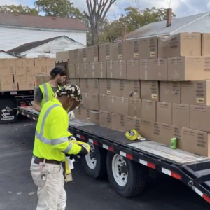 Trailers with stacked boxes in a parking lot, people in high-vis clothing around the trailers. 