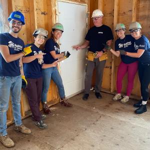volunteers posed inside a home being built, pointing to the door.